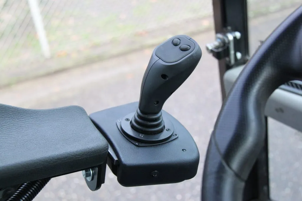 Ohjaussauvan joystick, jossa kaksi painiketta, asennettuna mustalle kiinnikkeelle ajoneuvon ohjaamon sisällä.