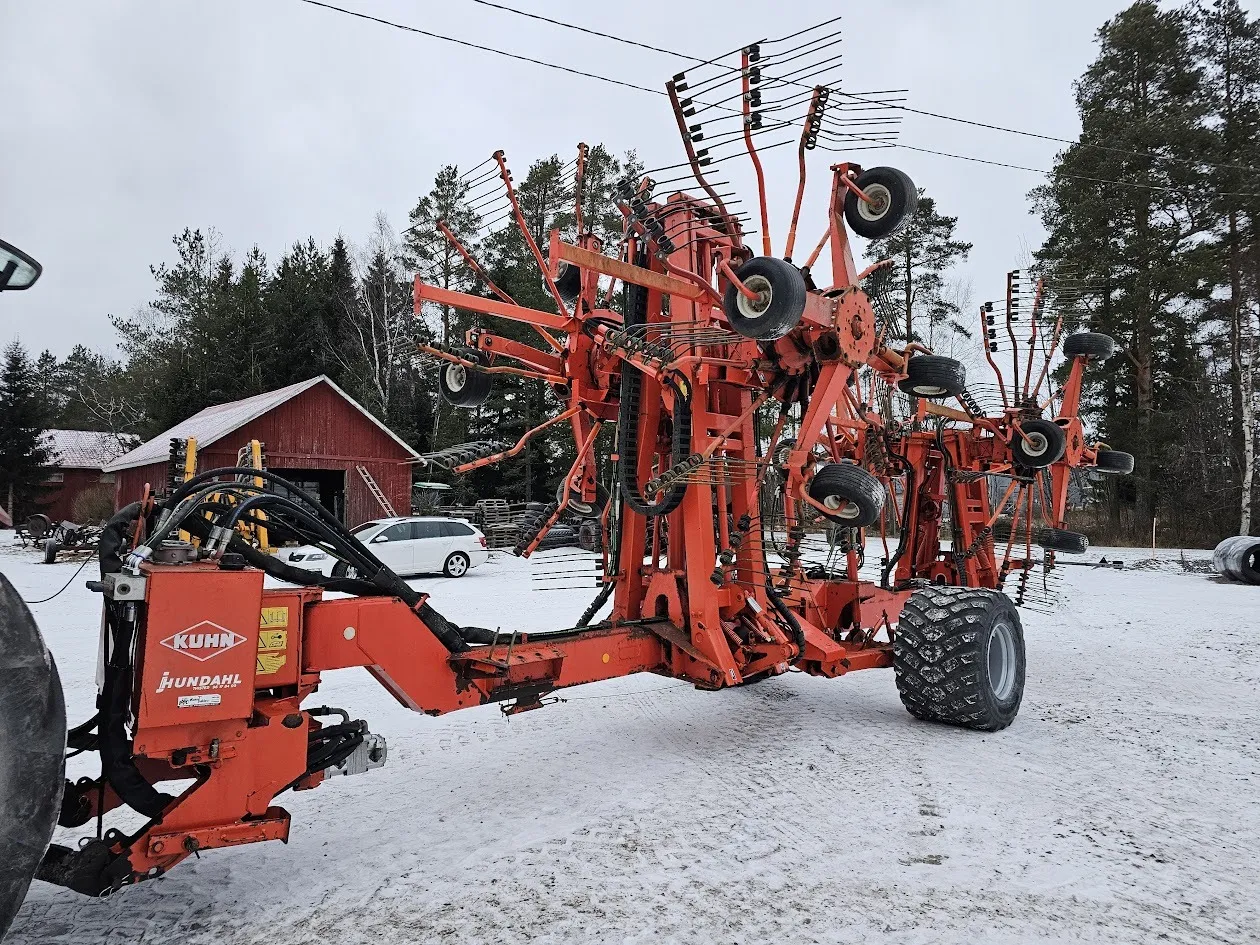 Punainen maatalouskone lumisella pihamaalla, taustalla metsää ja punainen lato.