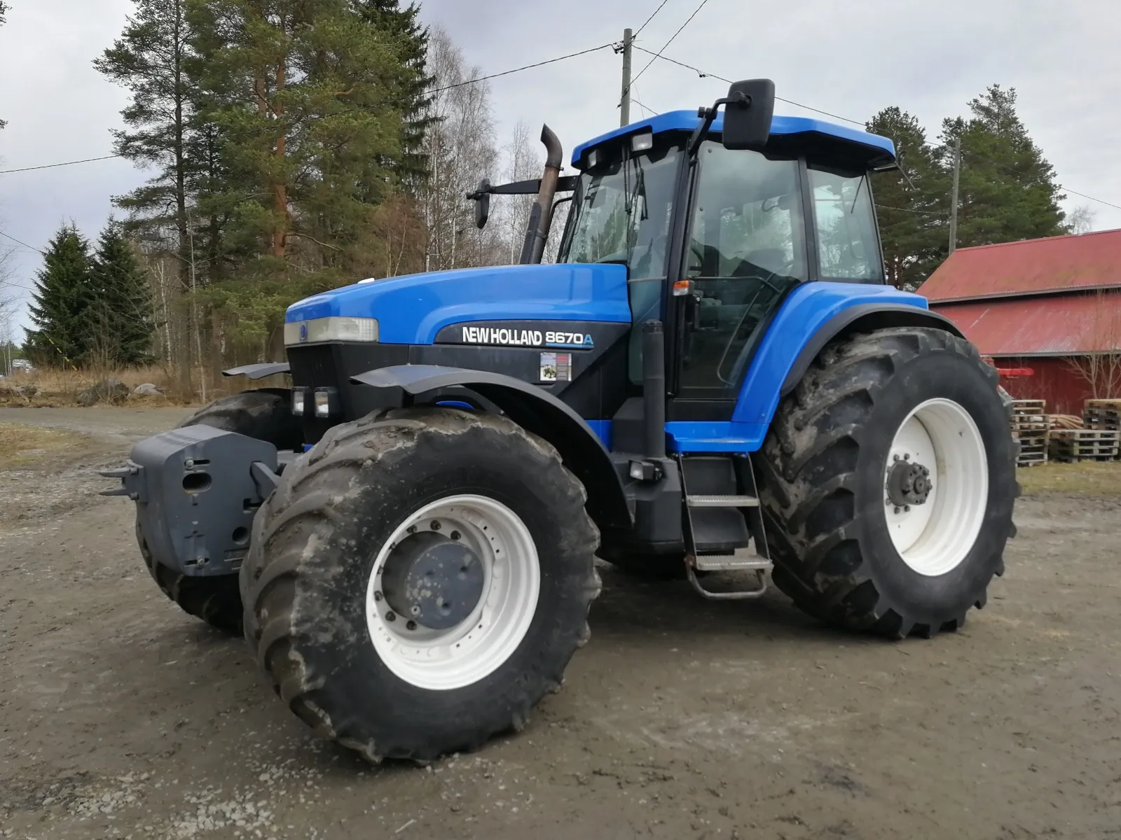 Sininen New Holland 8670A -traktori maantien laidalla metsäisen alueen vieressä.