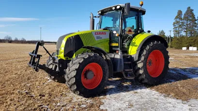 Vihreä CLAAS-puimuri isolla oranssilla renkaalla pellolla lumiseoksessa.