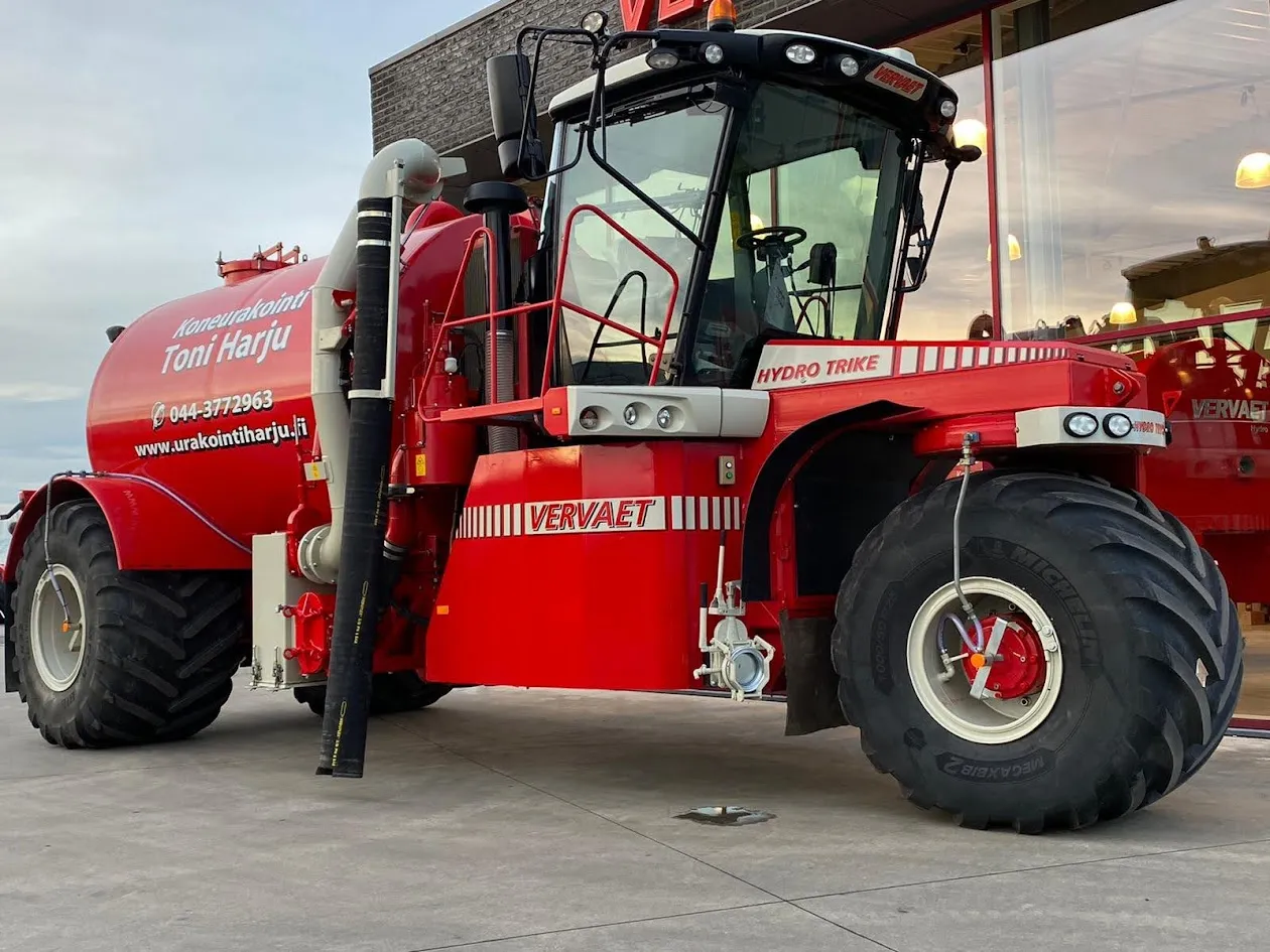 Punainen Vervaet Hydro Trike -maatalouskone, jossa iso säiliö ja suuret renkaat betonipinnalla rakennuksen edessä.