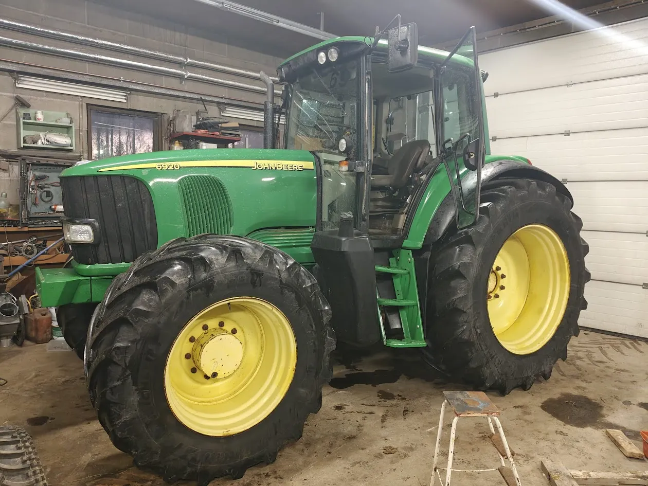 Vihreä John Deere 6920 traktori isoin keltaisin pyörin työkalujen ja tavaroiden täyttämässä tallissa.