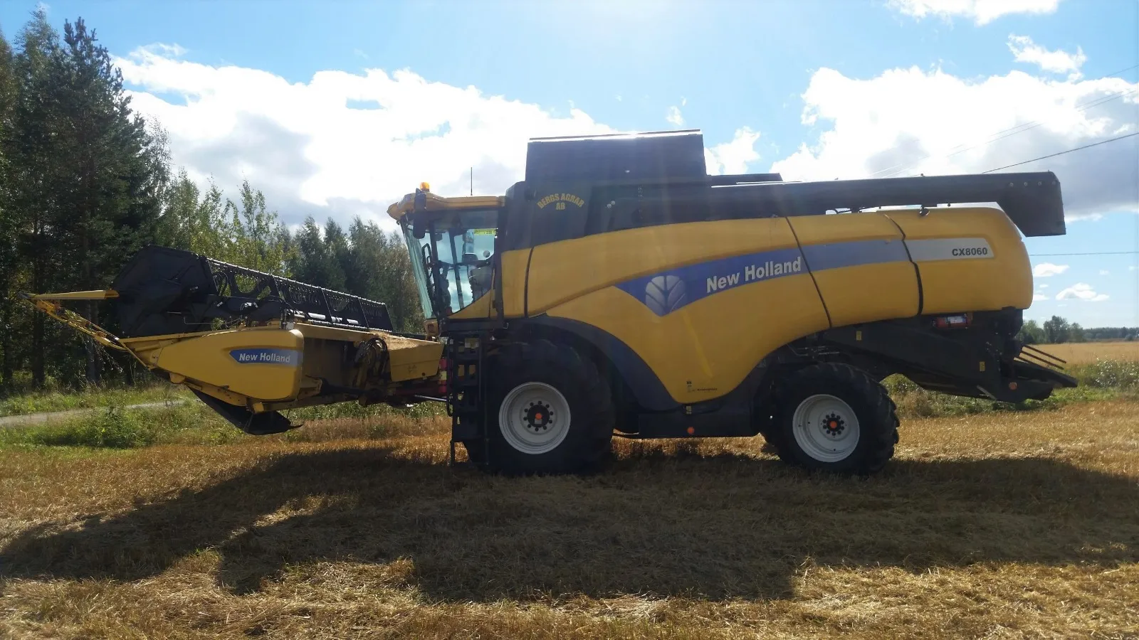Keltainen New Holland CX8060 -puimuri pellolla sinisen taivaan alla.