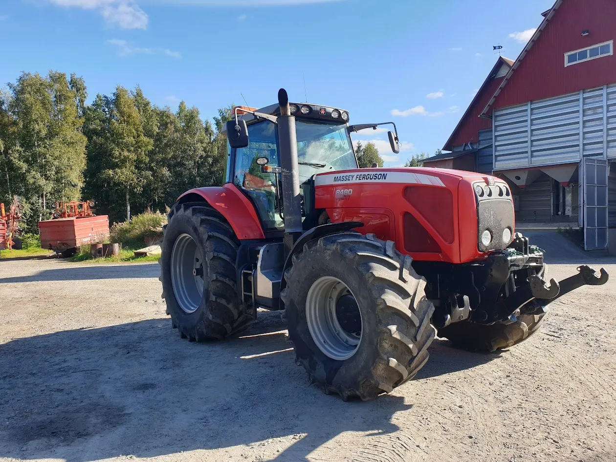 Punainen Massey Ferguson 8480 -traktori seisoo hiekkaisella pihalla, taustalla metsää ja maatilarakennuksia.