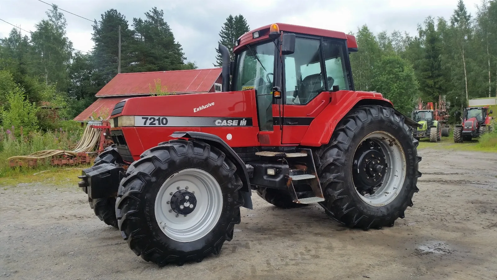 Punainen Case IH 7210 traktorikone maatalousympäristössä, taustalla puita ja muita traktoreita.