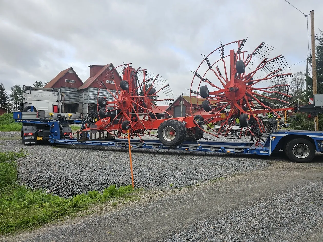 Maatalouskone, jossa on suuret punaiset pyörivät haravat, kuorma-autotrailerin päällä maaseutympäristössä.