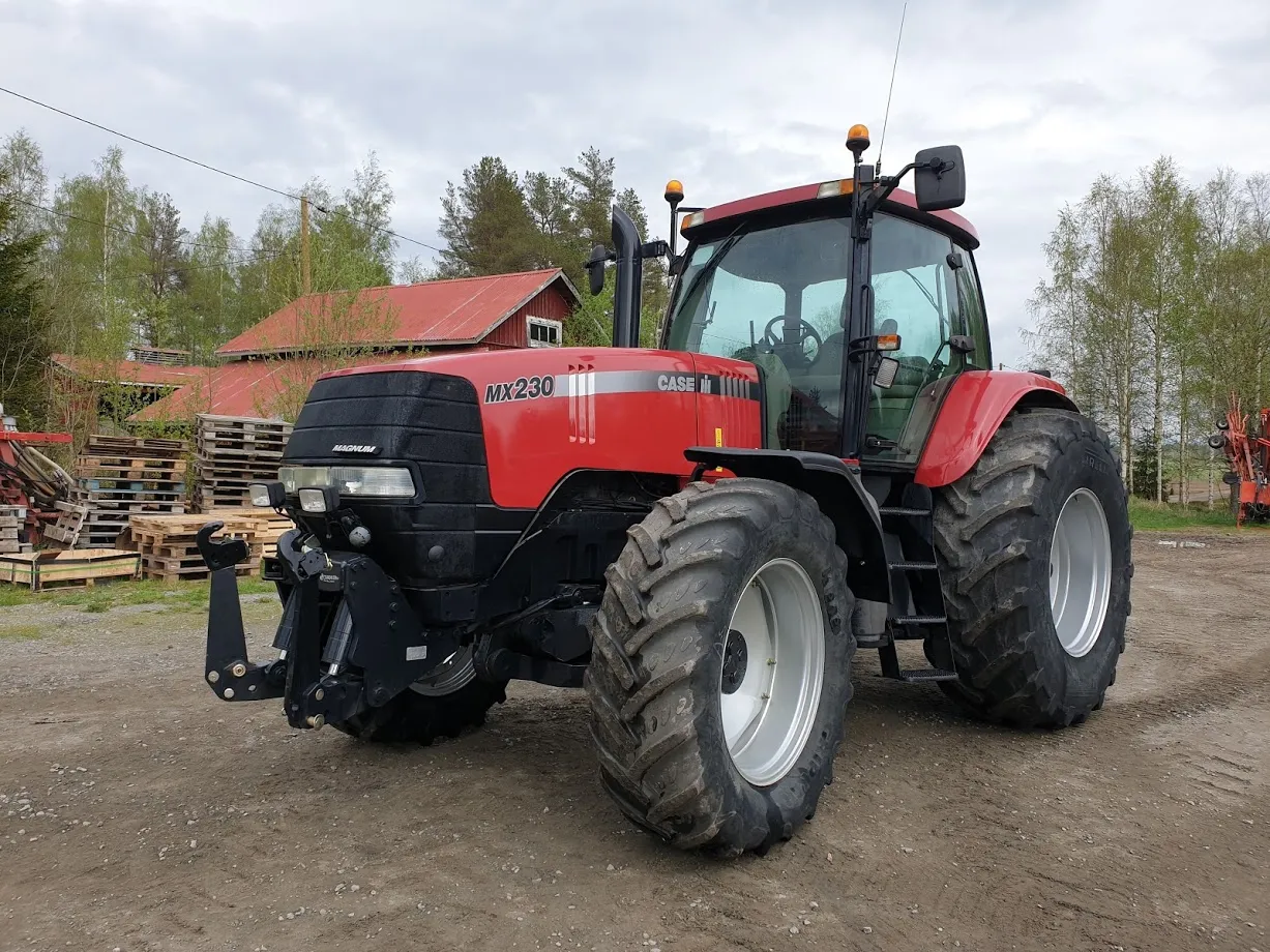 Punainen Case MX230 -traktori pihalla maatilan rakennusten ja puulavojen edessä.