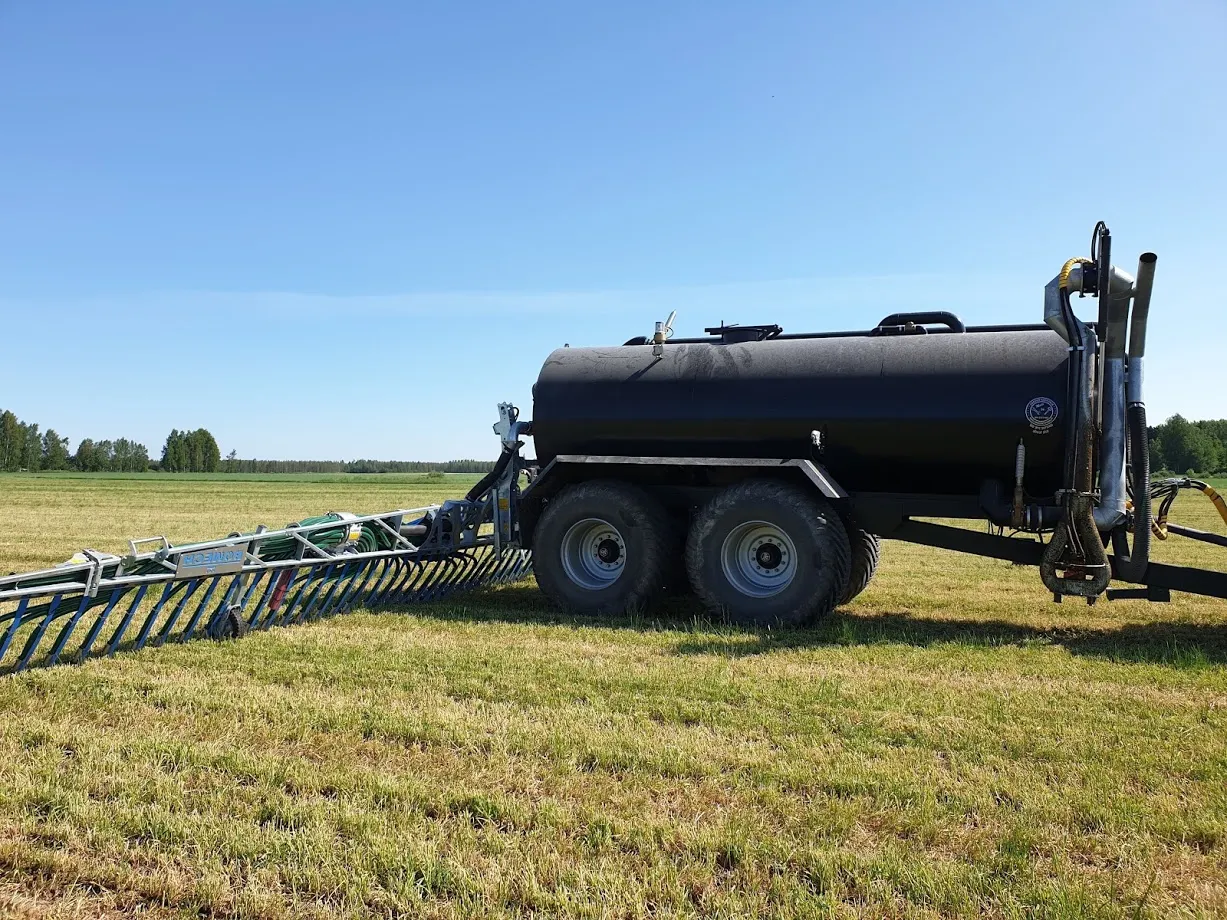 Musta lietevaunu ja levityslaite pellolla kirkkaana päivänä.