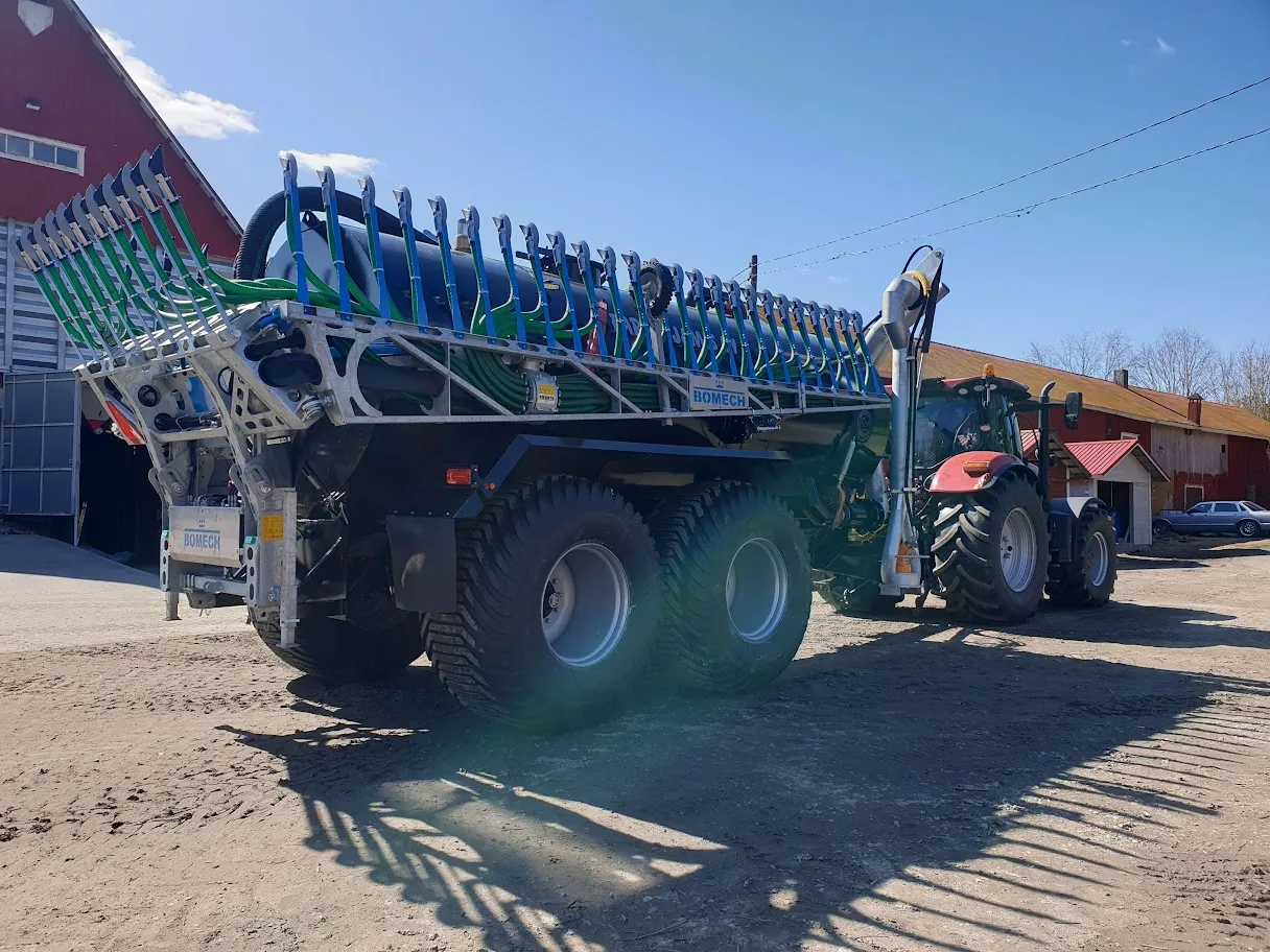 Traktori vetää Bomechin lannoitteenlevitintä maatilalla kirkkaana päivänä.