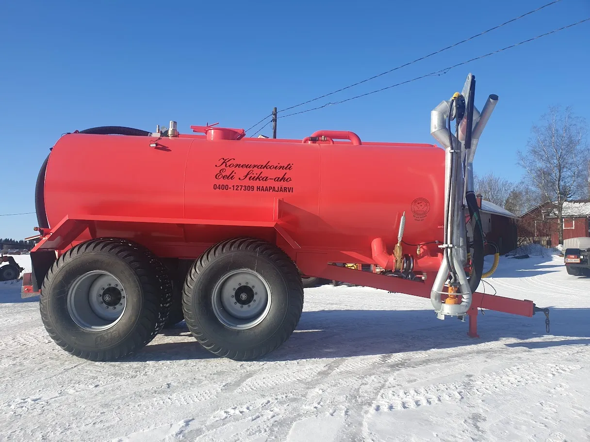 Punainen lietesäiliö, jossa mustat renkaat ja metalliaskelmat, lumisessa pihassa kirkkaalla taivaalla.