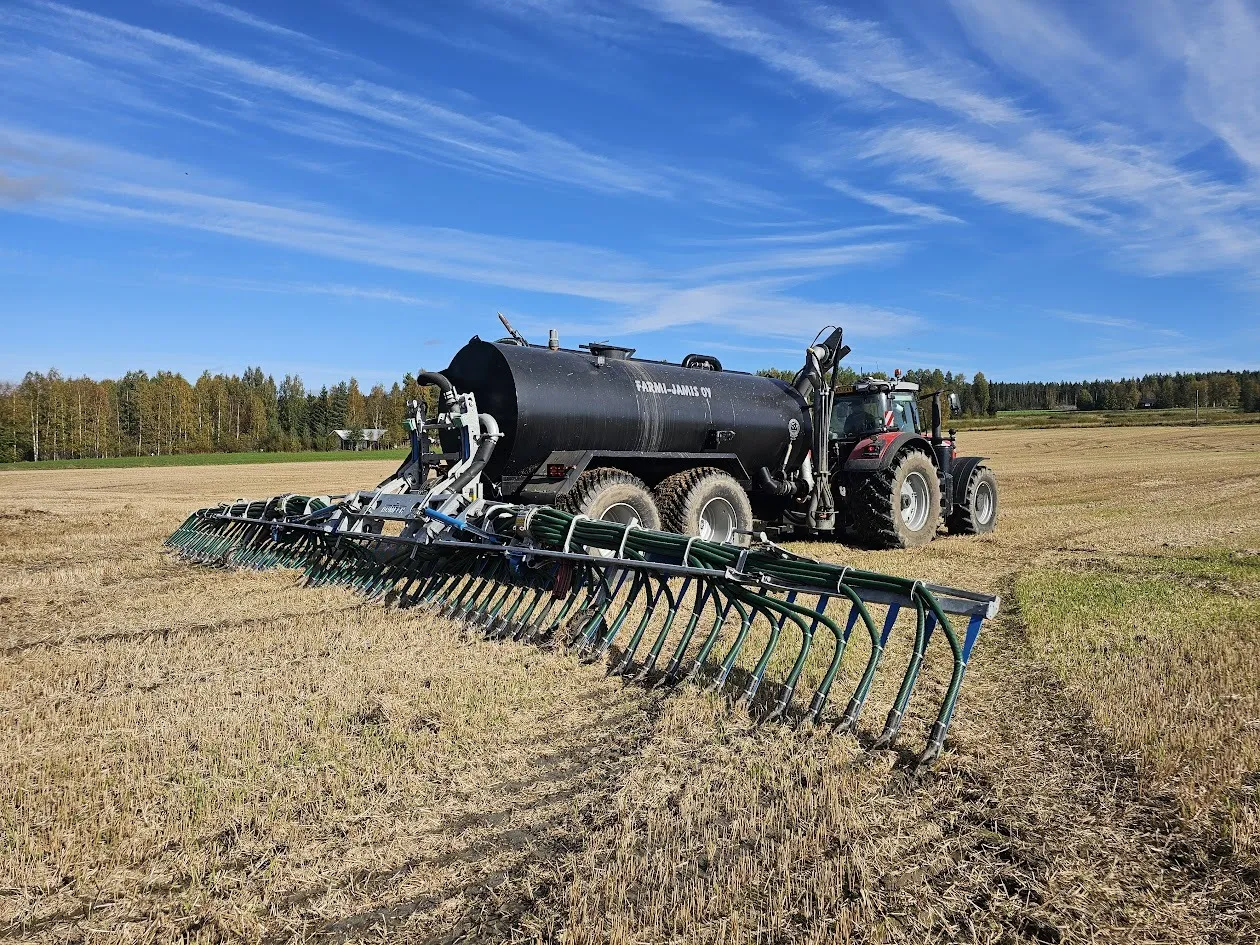 Traktori ja lietevaunu pellolla kirkkaalla sinisellä taivaalla.