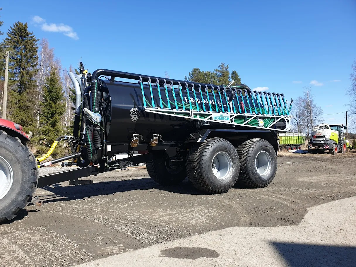 Musta lannoitevaunu kiinnitetty punaiseen traktoriin maatalousalueella sinisenä kirkkaana päivänä.