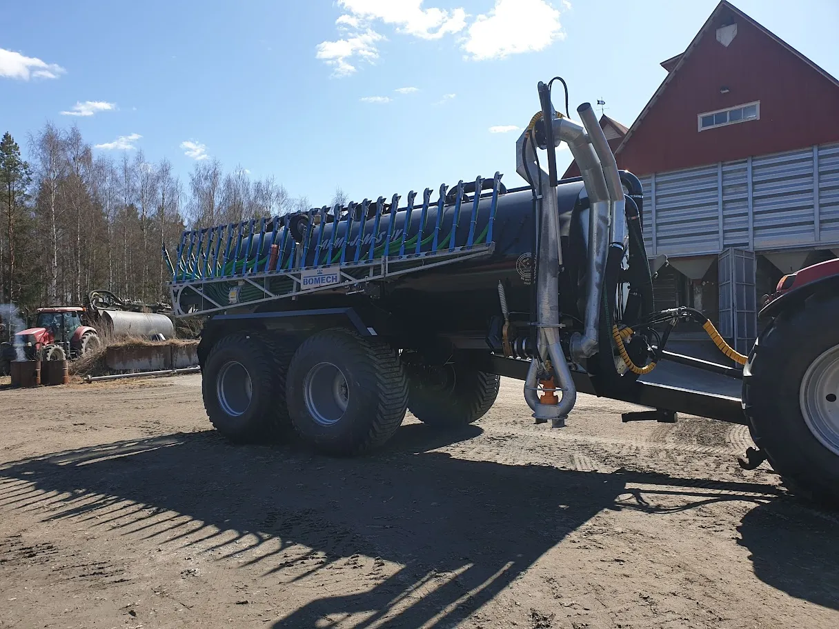 Musta ja sinivihreä Lietekarry Bomech -lannoitetynnyri kiinni punaisessa traktorissa maatilan pihalla.