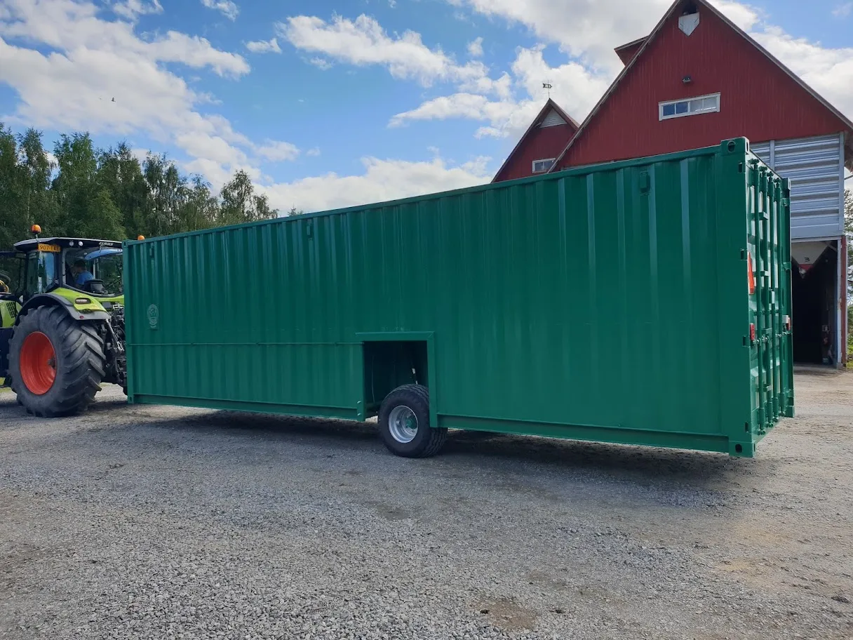 Vihreä kontti, jossa on pyörä alareunassa ja jonka vetää traktori maatilan pihalla.