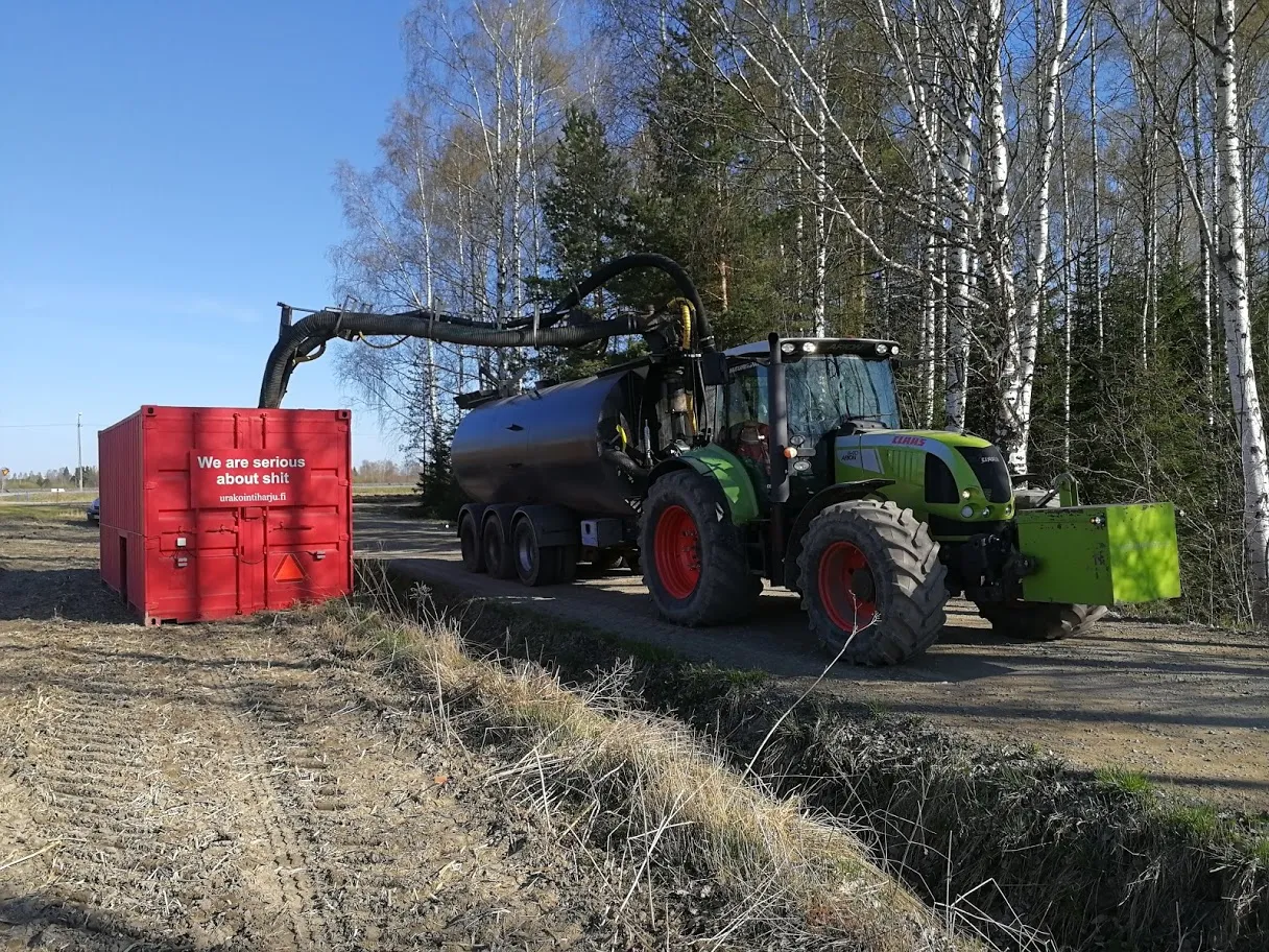 Traktori kiinnitettynä lietevaunuun, joka tyhjentää letkun kautta punaisen säiliön maaseutuympäristössä.