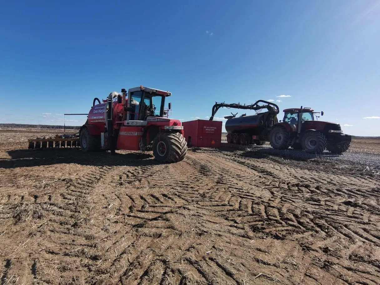Kaksi punaista maatoukon konetta maassa, taustalla kirkas sininen taivas.