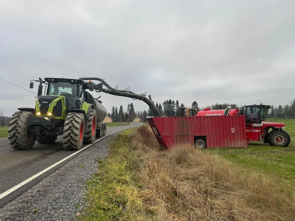 Traktori vetää lietekonttia maantien vieressä, lietepumppu pumppaa lietettä kontista traktoriin.