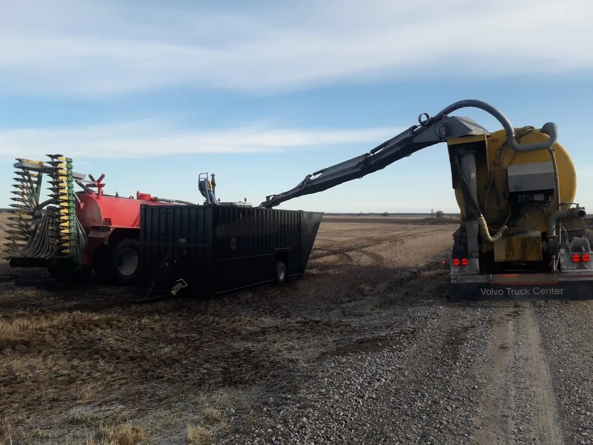 Maatalouskoneita, joista yksi on punainen lannoitteenlevitin ja toinen keltainen perävaunu, jotka ovat pellolla ja lastaavat materiaalia mustaan säiliöön.