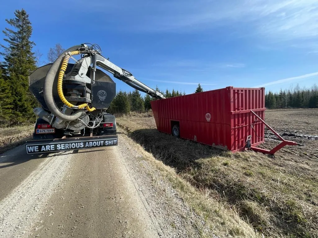 Säiliöauto ja punainen lietjekontti pellon laidalla aurinkoisena päivänä.