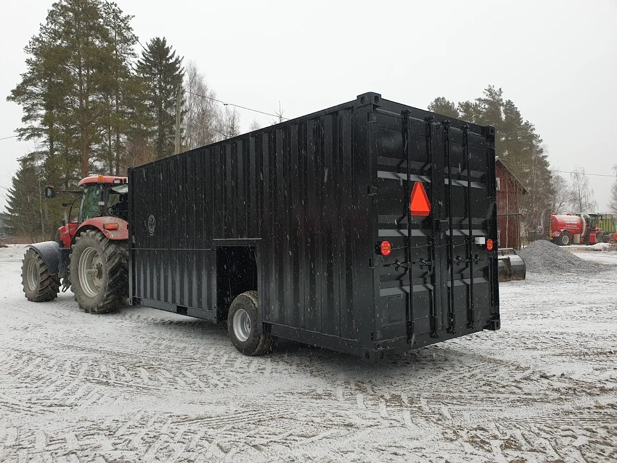 Punainen traktori vetää mustaa maatalouskonttia lumisella pihamaalla.