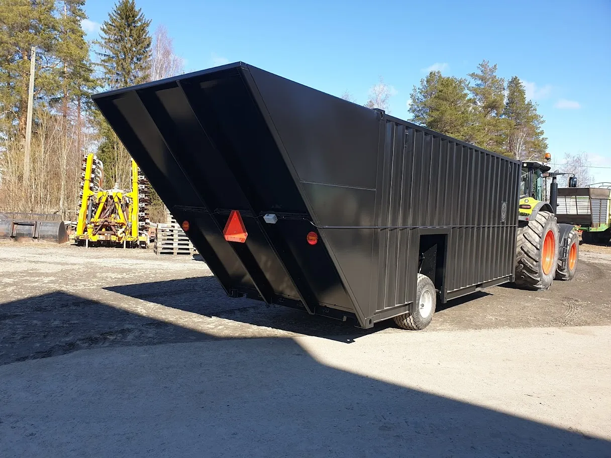 Iso musta lietekontti kiinnitettynä traktoriin ulkona pihalla aurinkoisena päivänä.