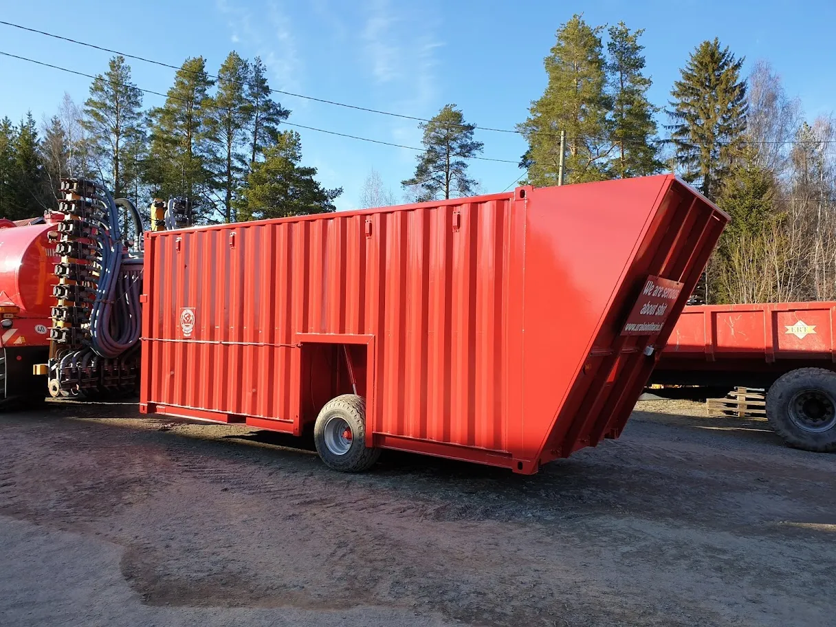 Punainen lietekontti, jossa yksi pyörä, pysäköity ulkona metsän vieressä.