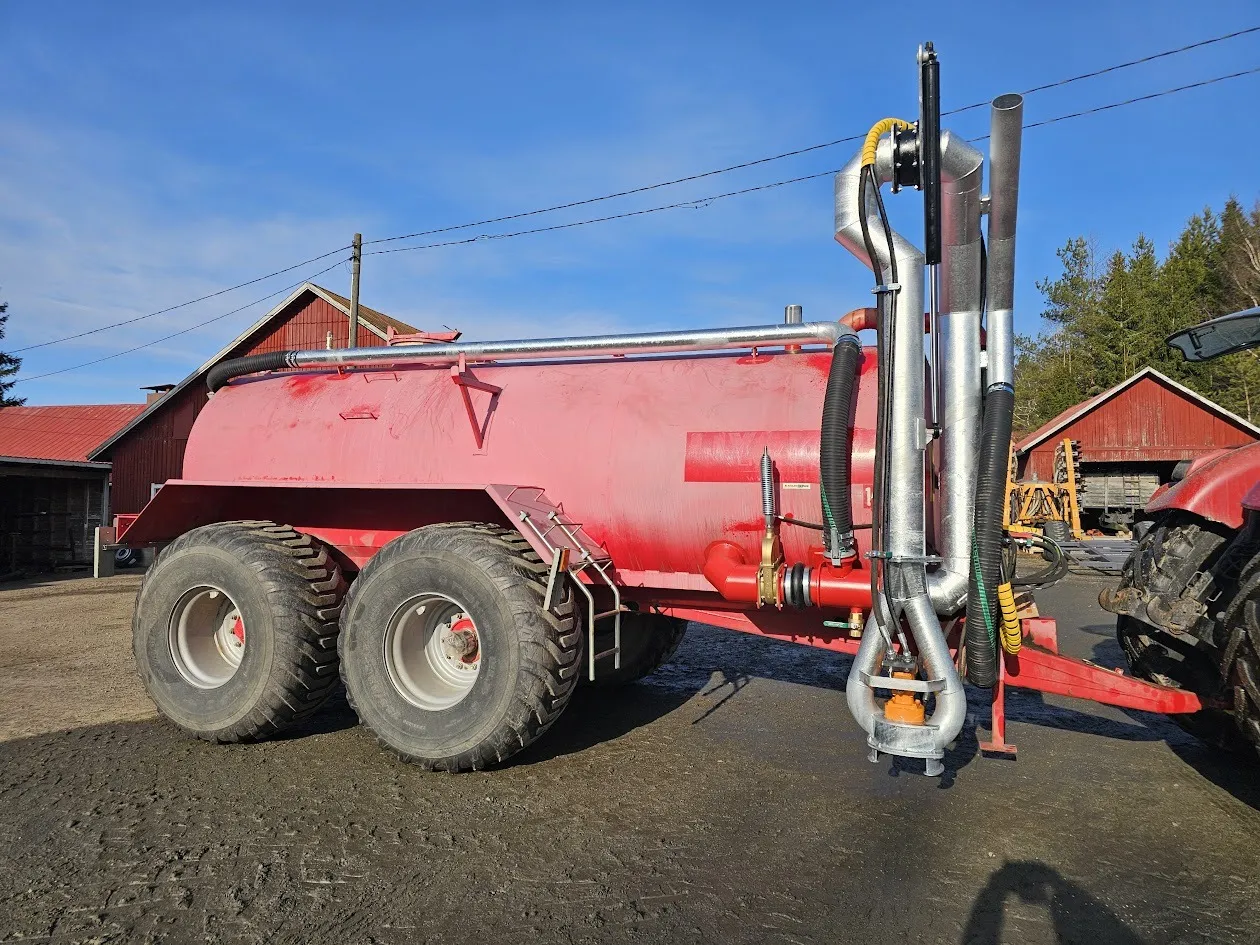 Punainen lietelantavaunu isolla kaksoispyörästöllä, kiinnitettynä traktoriin maatilalla.