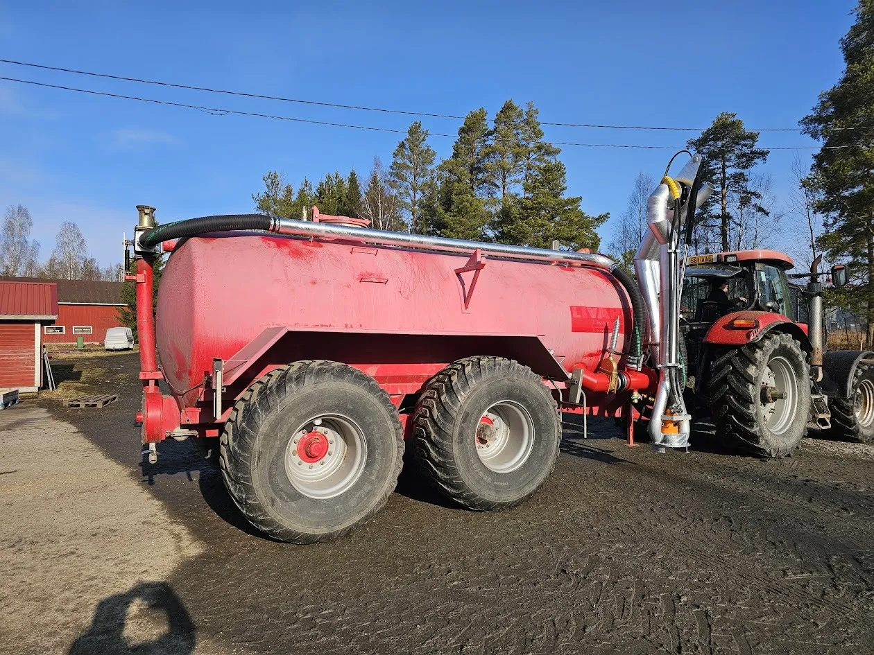 Punainen lietelantavaunu traktorin perässä aurinkoisena päivänä maatalousympäristössä.