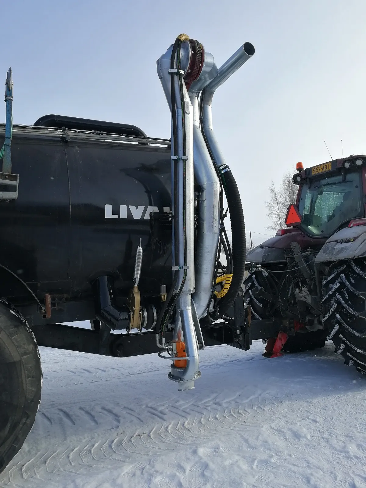 Punainen traktori kiinnitetty mustaan lietesäiliöön lumisella pellolla.