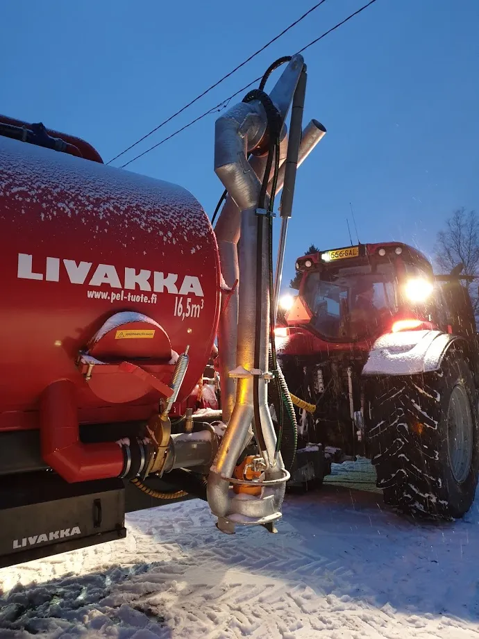 Punainen Livakka säiliövaunu kiinnitettynä traktoriin lumisella pihalla hämärässä.