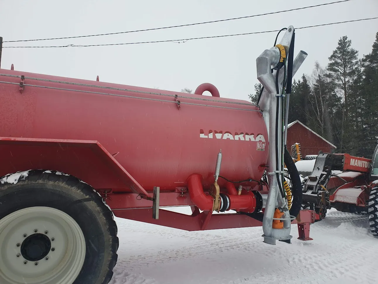 Punainen Livakka-merkkinen 16,5 kuution tilavuinen säiliövaunu lumisessa pihassa, kytketty traktoriin.