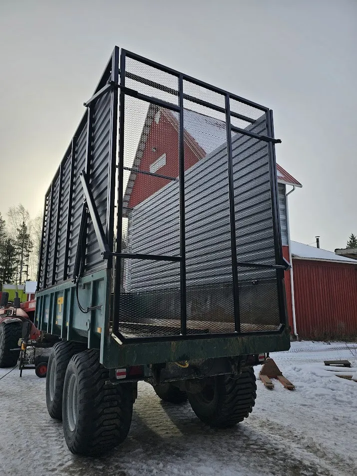 Traktoriin kytketty suuri maastorenkailla varustettu maansiirtovaunu lumisella pihamaalla.