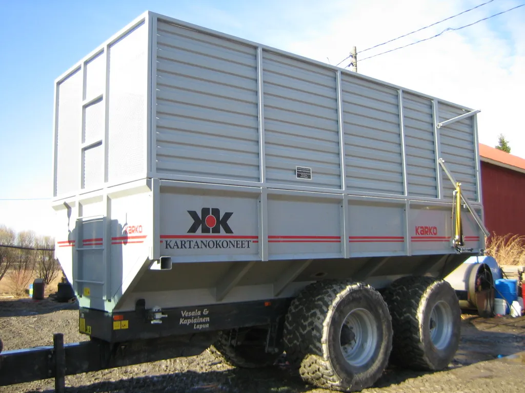 Vaaleanharmaa Agriculturen perävaunu, jossa keltaisia ja punaisia merkintöjä, kaksipyöräinen nastarenkailla.