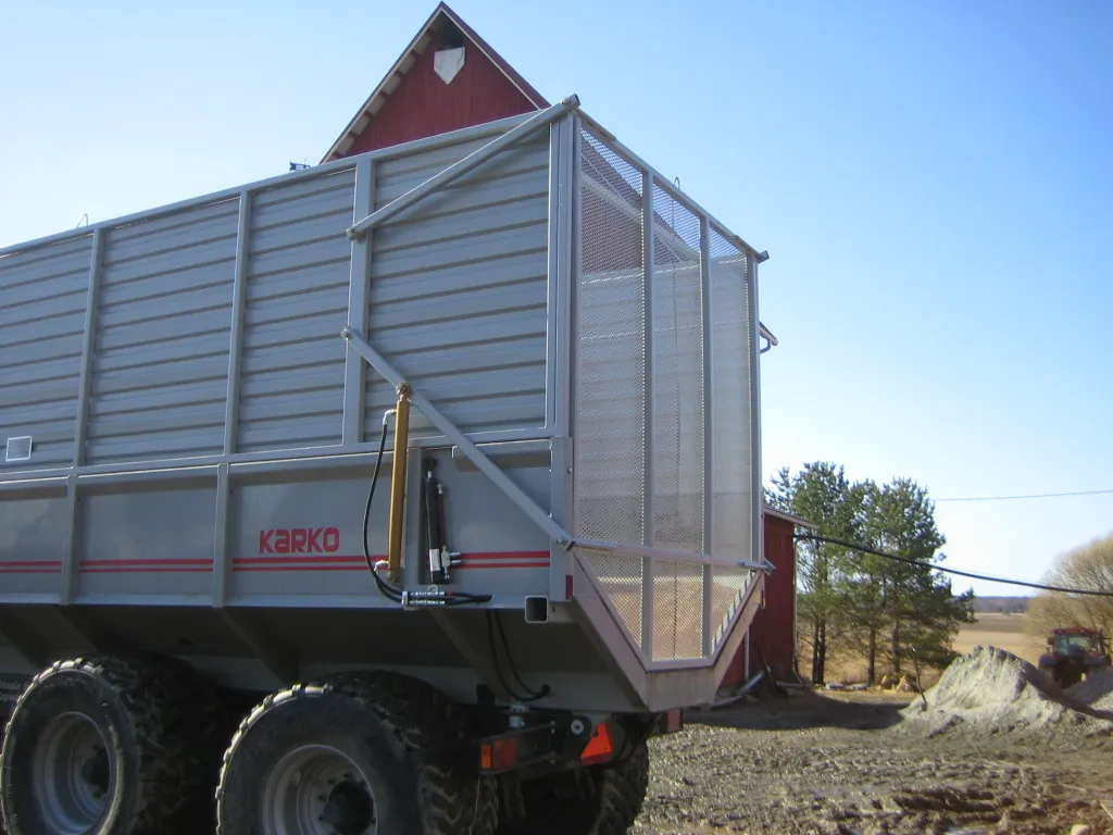 Maastoajoon suunniteltu iso harmaa Karko-perävaunu punaisen maalaistalon edessä kirkkaana päivänä.