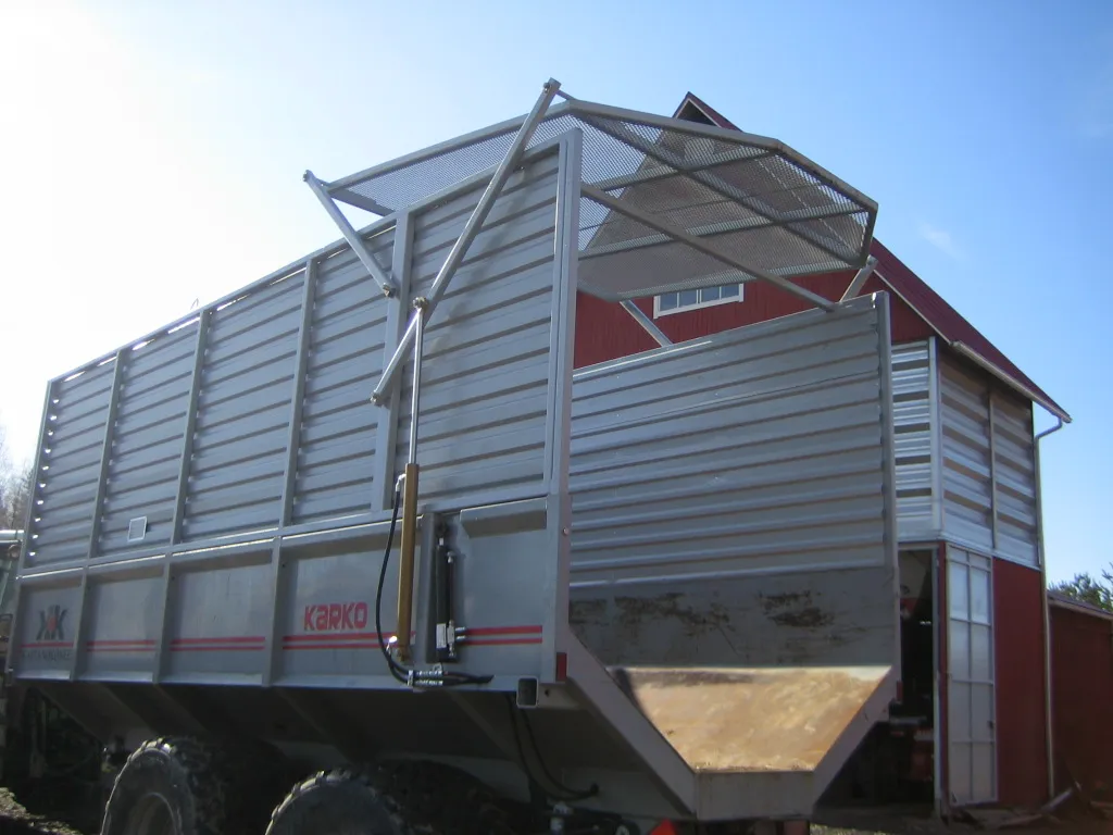 Teollinen metallinen karjakärry parittain suurilla renkailla maatilan rakennuksen edessä.